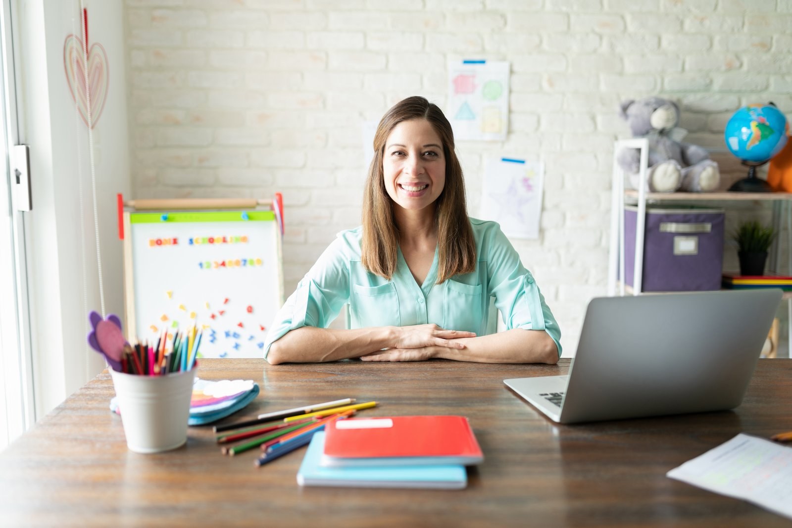 A teacher at her desk with a laptop and coloured pencils