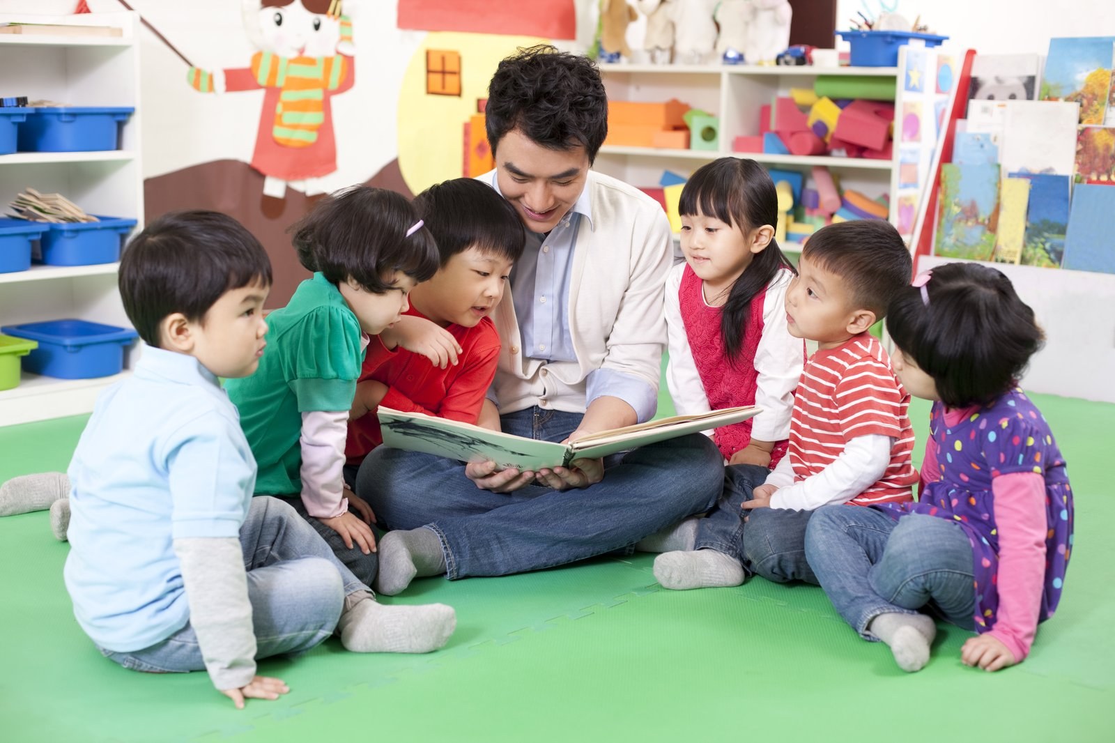 A teacher reading to children on a mat
