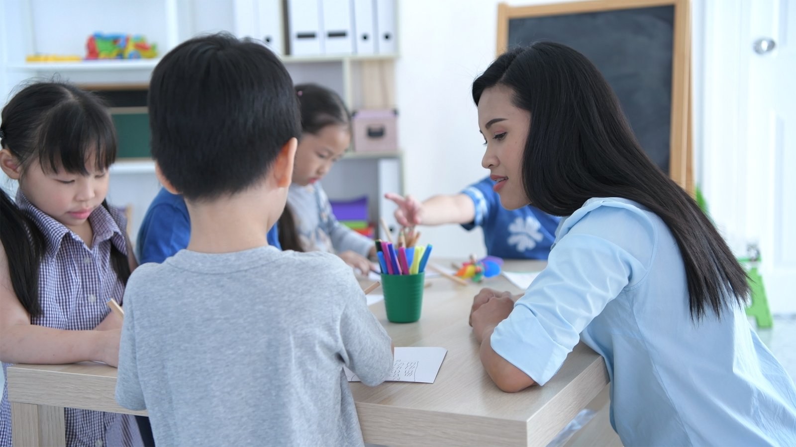 A teacher helping children draw at a classroom table